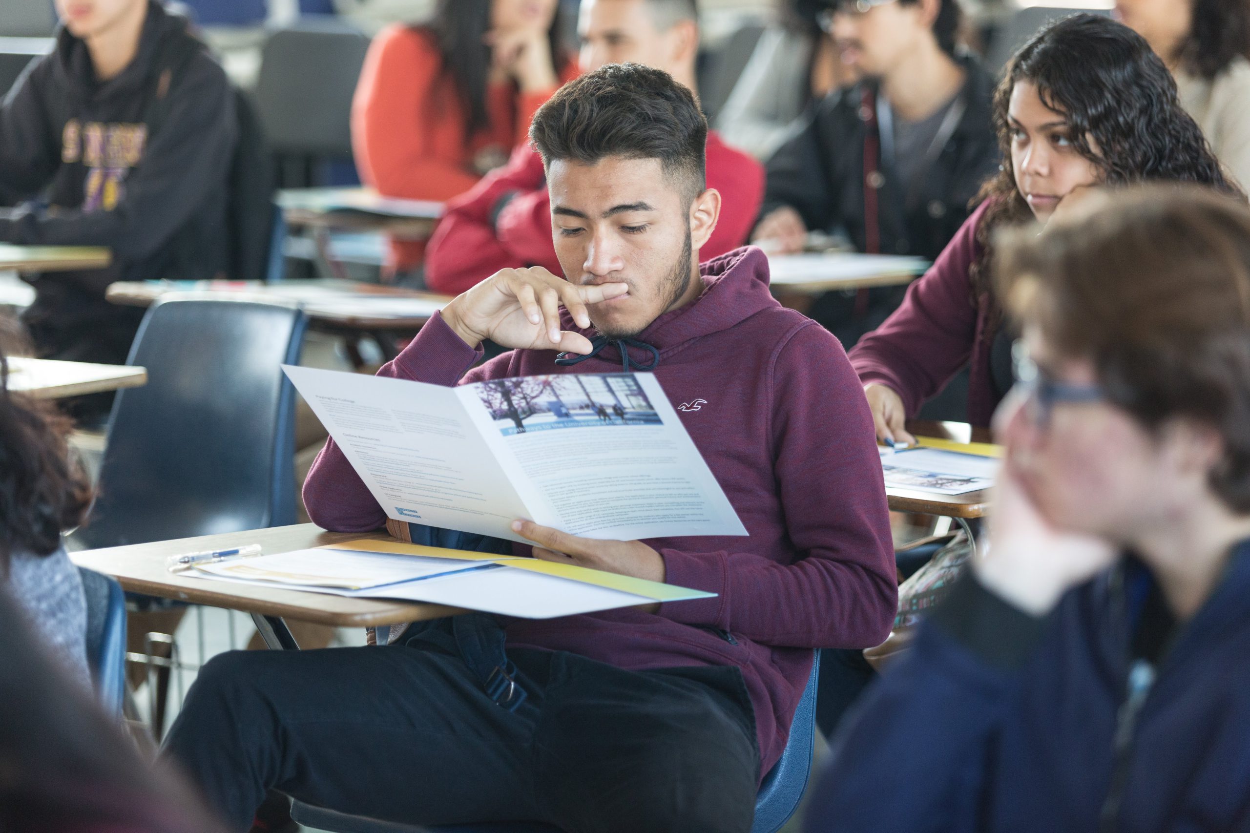 High schooler reading a brochure about a UC program to prepare for college.